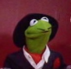 A Muppet frog wearing a fake mustache, a neckerchief, a suit, and a fedora